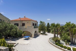 A stone building with a red-tiled roof, a courtyard with a ping pong table, and palm trees. - Villa Freedom | A Private Luxury Estate in the Heart of Crete (Chania)