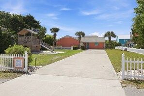 A pathway leading to a building with a red facade, a wooden structure resembling a boat, and a white picket fence. - Coral Cay - Oceanside home (Emerald Isle)