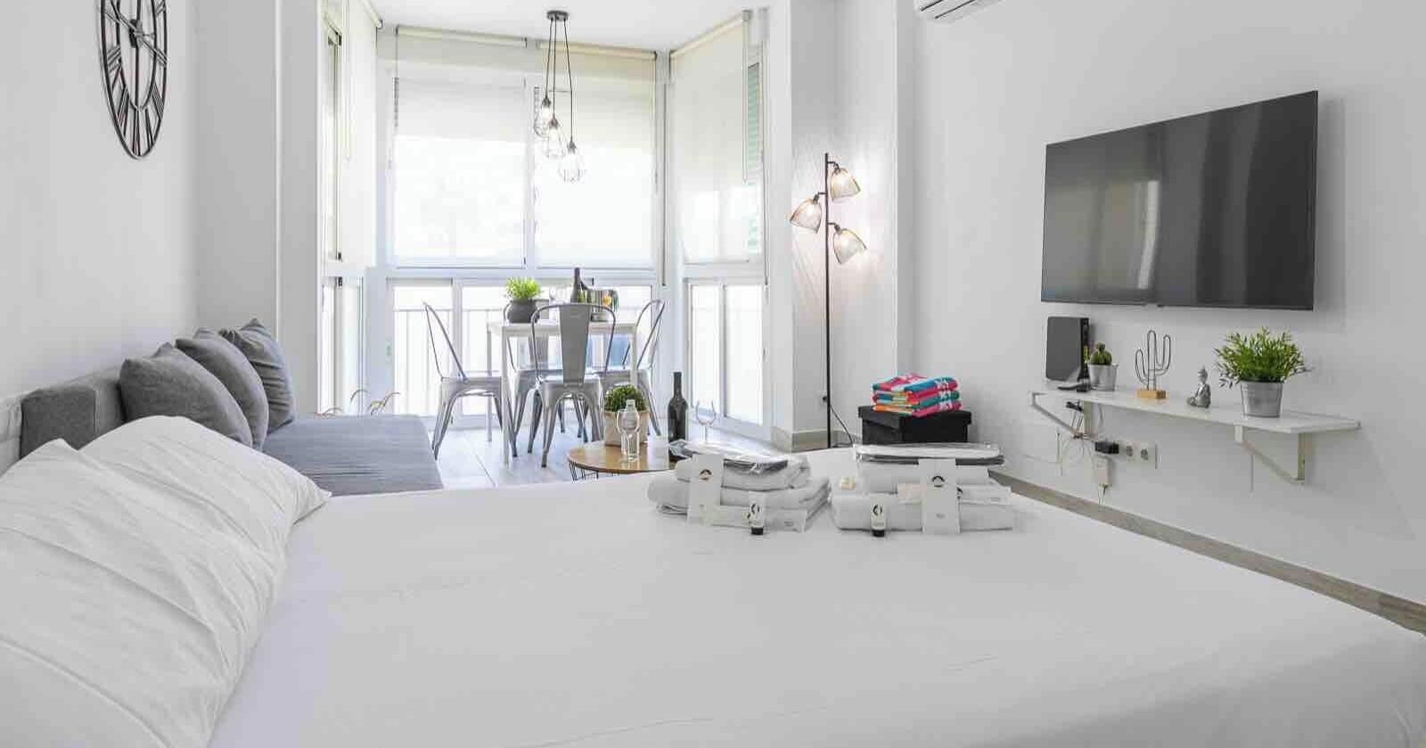Un dormitorio moderno con una cama grande, un televisor montado en la pared y un balcón con zona de comedor.