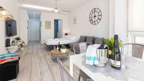 Ein modernes Wohnzimmer mit einer Couch, einem Esstisch und einer Champagnerflasche sowie einer Wanduhr.