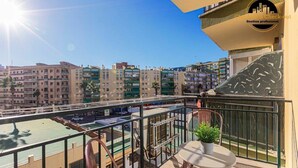 Ein Balkon mit Tisch und Stühlen, einem kleinen Blumentopf und Blick auf eine Stadtlandschaft mit mehreren Gebäuden.