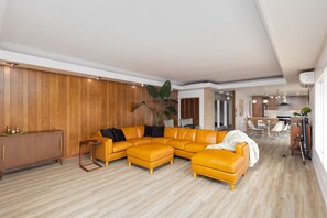 A modern living room with a sectional sofa, wooden panel walls, and a dining area with a table and chairs. - Bay View Dunes Getaway (North Bend)