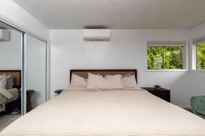 A bedroom with a bed, bedside tables, a nightstand, a green chair, and a window with a view of greenery. - Bay View Dunes Getaway (North Bend)