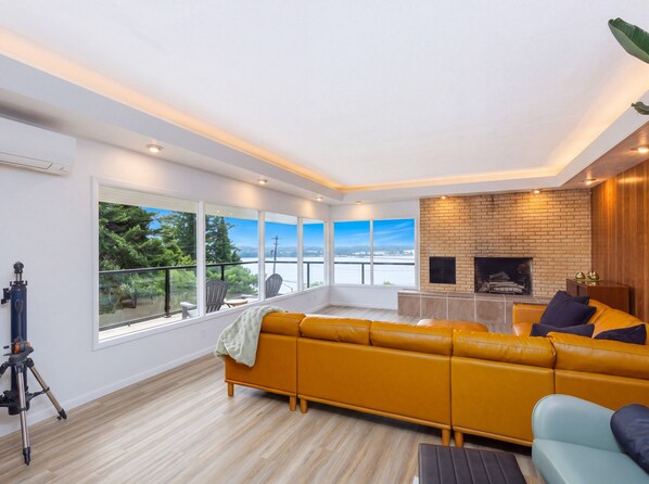 A modern living room with a large sofa, a fireplace, and a balcony with a view. - Bay View Dunes Getaway (North Bend)