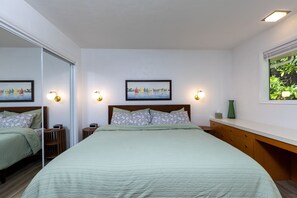 A bedroom with a bed, bedside tables, a mirror, a painting, and a window with a view of greenery. - Bay View Dunes Getaway (North Bend)