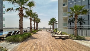 A rooftop lounge area with a wooden deck, palm trees, and lounge chairs. - Elegant Studio Retreat in Damac Hills (Dubai)