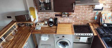 Une cuisine compacte équipée d’un lave-linge, d’un four et d’une machine à café posée sur le plan de travail.