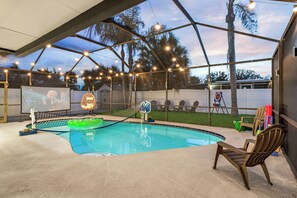 An outdoor swimming pool with a netted area, surrounded by chairs and a covered seating area with string lights. - Tampa Pool Oasis, Lux Boho Design, , Otdr Movie & Kitchen, Near Golf (Tampa)