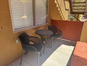 A small outdoor seating area with two chairs and a table, a window with blinds, and a staircase visible in the background. - Hawks Nest | 2BR, Ground, 3miles to Sports Complex + Free Perks (Mesquite)