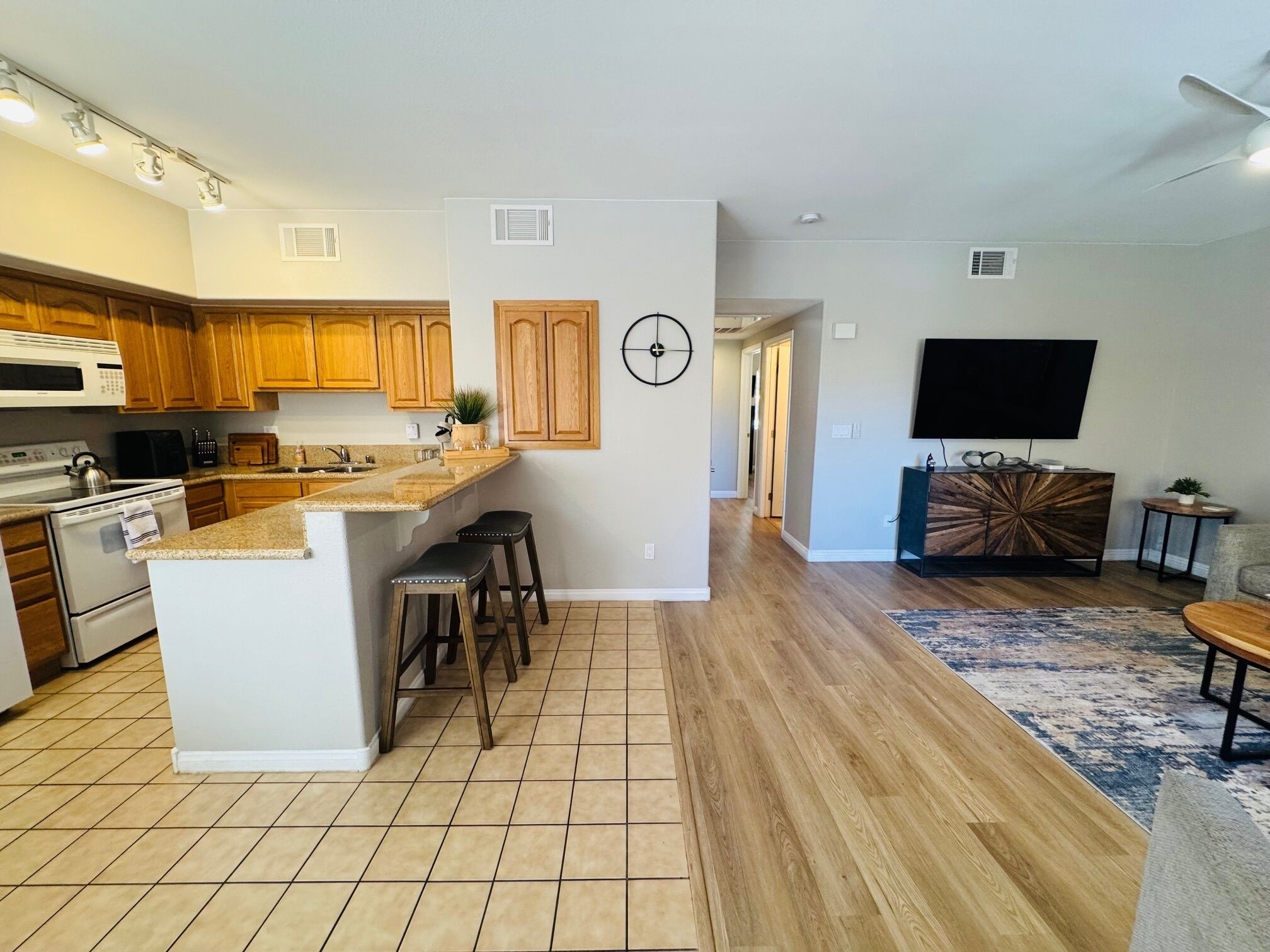 A modern kitchen with wooden cabinets, a central island, and a dining area with a TV and seating.