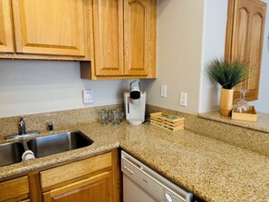 A kitchen with wooden cabinets, a stainless steel sink, a coffee maker, and a dishwasher. - Hawks Nest | 2BR, Ground, 3miles to Sports Complex + Free Perks (Mesquite)