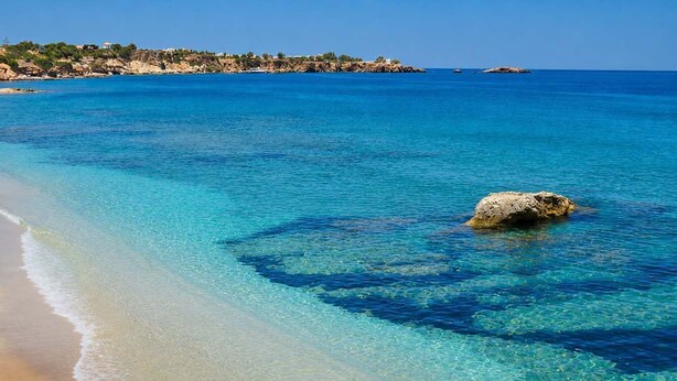 Una spiaggia con acque cristalline color turchese, una riva sabbiosa e affioramenti rocciosi.