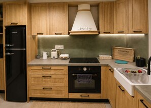 A modern kitchen with wooden cabinets, a black refrigerator, a stove, and a sink with a serving tray. - A2 Maisonette - Modern Cretan Living by the Sea (Limenas Chersonisou)