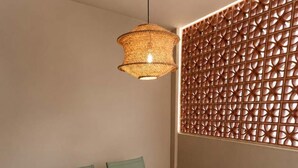 Un'area pranzo con tavolo imbandito per quattro persone, sedie verdi, una lampada a sospensione intrecciata e un pannello decorativo con motivo geometrico.