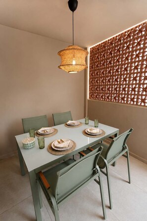 A dining area with a table set for four, green chairs, a woven pendant light, and a decorative panel with a geometric pattern. - A2 Maisonette - Modern Cretan Living by the Sea (Limenas Chersonisou)