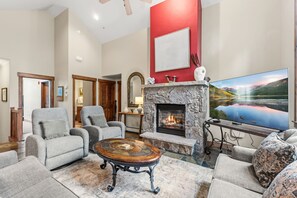 A living room with a stone fireplace, comfortable seating, a flat-screen TV, and a large window with a scenic view. - Walk to Gondola | Mountain Thunder Townhome Retreat (Breckenridge)