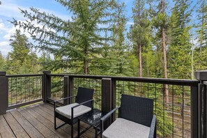 A wooden deck with two chairs and a table, surrounded by a metal railing, overlooking a forested area. - Walk to Gondola | Mountain Thunder Townhome Retreat (Breckenridge)