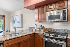 A kitchen with granite countertops, wooden cabinets, stainless steel appliances, and a painting on the wall. - Walk to Gondola | Mountain Thunder Townhome Retreat (Breckenridge)