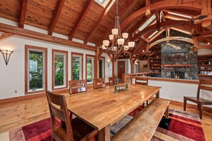 A spacious dining area with a wooden table and chairs, large windows, and a stone fireplace. - Bottle Bay Lakefront Lodge | Dock & Game Room (Sagle)