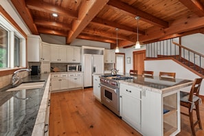 A kitchen with wooden beams, white cabinets, a stove, and a dining area with chairs. - Bottle Bay Lakefront Lodge | Dock & Game Room (Sagle)