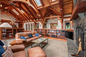 A spacious living room with a high wooden ceiling, a fireplace, and a cozy seating area with a leather sofa and ottoman. - Bottle Bay Lakefront Lodge | Dock & Game Room (Sagle)