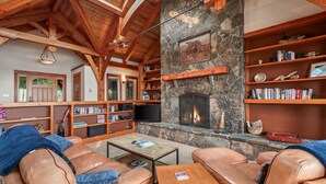 Ein gemütliches Wohnzimmer mit Ledersofas, einem Kamin aus Stein, Holzregalen und einem Fernseher.