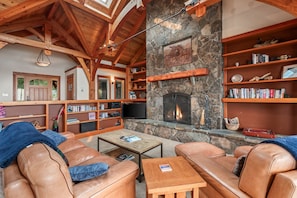 A cozy living room with leather sofas, a stone fireplace, wooden bookshelves, and a television. - Bottle Bay Lakefront Lodge | Dock & Game Room (Sagle)
