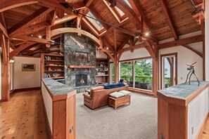 A spacious living area with a stone fireplace, wooden beams, and large windows.