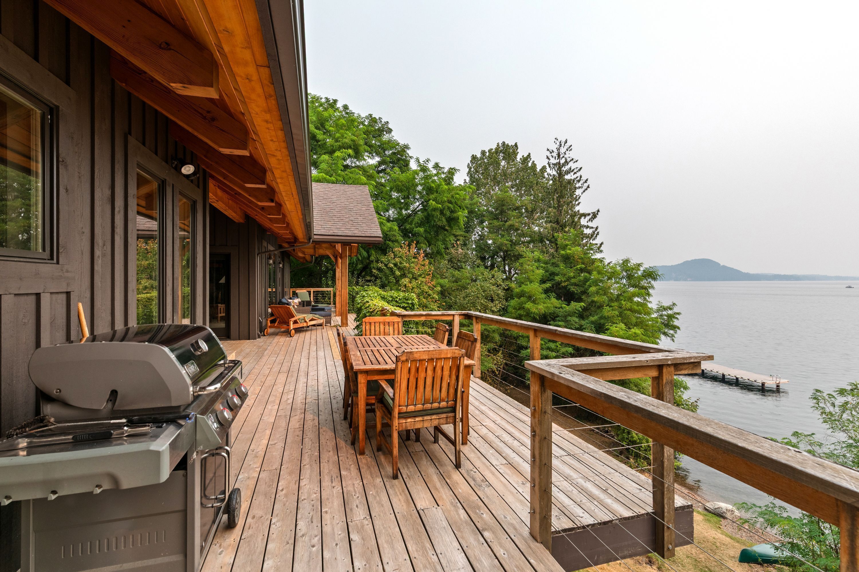 A wooden deck with outdoor furniture, a grill, and a view of a lake.