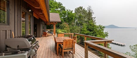 A wooden deck with outdoor furniture, a grill, and a view of a lake.