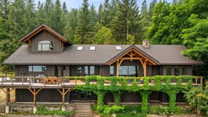 Ein modernes, zweistöckiges Haus mit Terrasse, großen Fenstern und einer Veranda mit Kletterpflanzen.