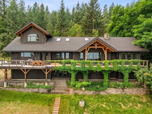 A modern two-story house with a deck, large windows, and a covered porch with climbing vines. - Bottle Bay Lakefront Lodge | Dock & Game Room (Sagle)