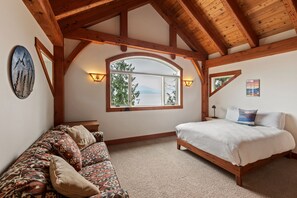 A bedroom with a large window, wooden beams, a bed, a sofa, and a wall-mounted lamp. - Bottle Bay Lakefront Lodge | Dock & Game Room (Sagle)
