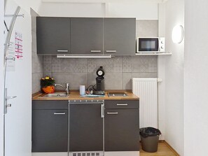 Eine kleine Küche mit grauen Schränken, einer Mikrowelle, einer Kaffeemaschine und einem Mülleimer.