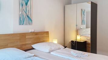 A hotel room with a wooden headboard, a bed with white linens, a bedside table with a lamp, and a large mirror reflecting the room.