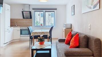 A compact living space with a kitchenette, dining area, and a sofa with red cushions.