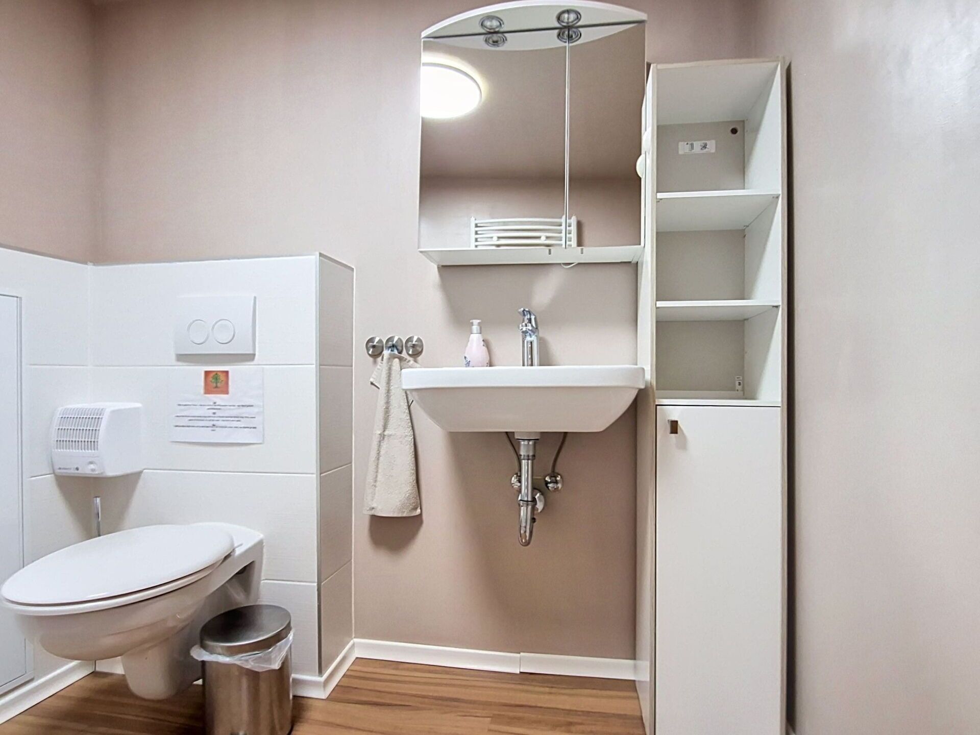 A bathroom with a toilet, sink, mirror, and a small shelf.