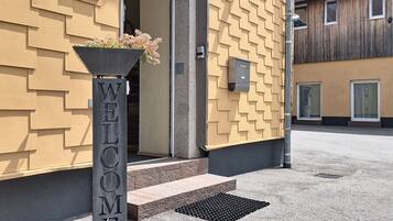 A building entrance with a 'WELCOME' sign, a planter with flowers, and a mailbox.