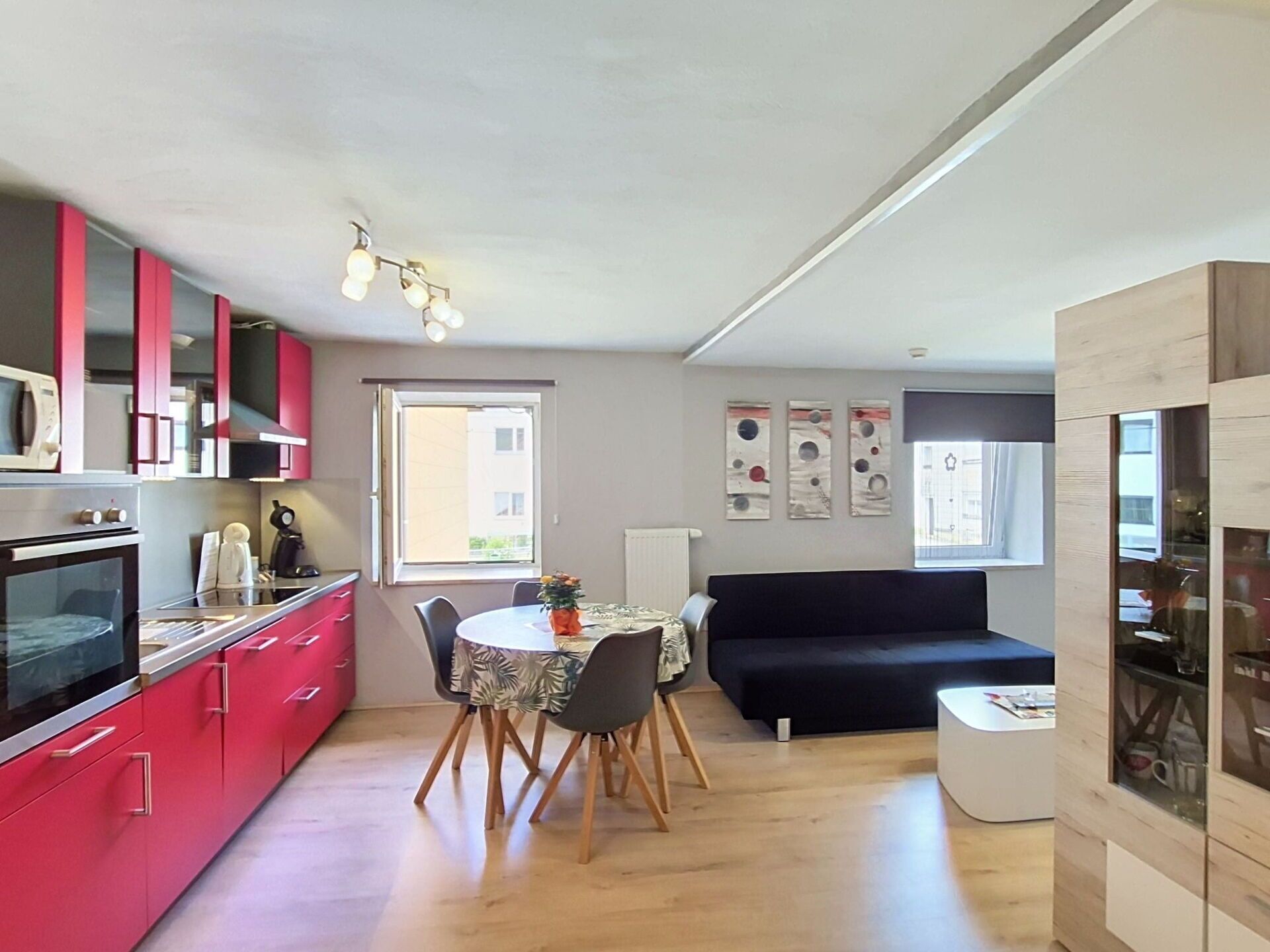 Una cocina compacta con electrodomésticos modernos, un comedor con una mesa redonda y un sofá negro.