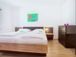 Habitación de hotel con cama doble, mesita de noche con lámpara, cómoda y un cuadro en la pared.