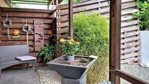 Un patio couvert agrémenté d’une clôture en bois, d’un banc, d’un jardinier avec des fleurs et de décorations murales.