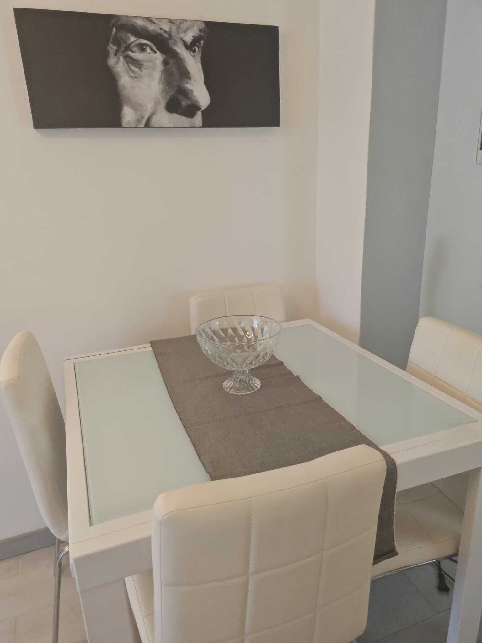 A dining area with a glass table, a central glass bowl, and white chairs.