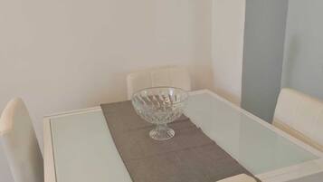 A dining area with a glass table, a central glass bowl, and white chairs.