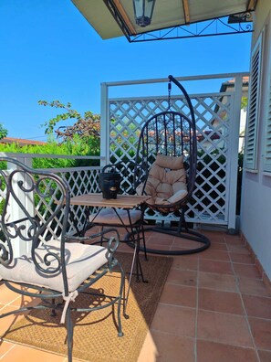 A patio with a hanging chair, a table, and a metal chair. - Apartment with a private pool and garden, just a few minutes from the beach (Pietrasanta)
