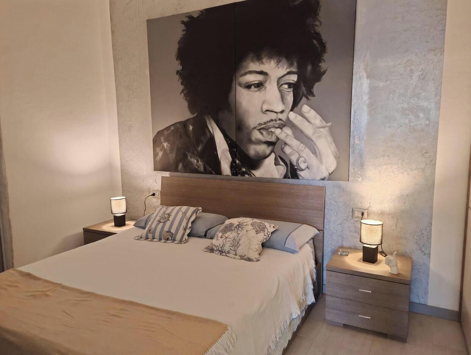 Un dormitorio con una cama grande, dos mesitas de noche con lámparas, un cabecero y una obra de arte grande en la pared.