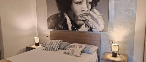 Un dormitorio con una cama grande, dos mesitas de noche con lámparas, un cabecero y una obra de arte grande en la pared.