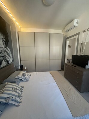 A bedroom with a bed, a dresser, a television, and an air conditioning unit. - Apartment with a private pool and garden, just a few minutes from the beach (Pietrasanta)