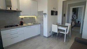Uma cozinha moderna com armários brancos, fogão a gás e um espaço de refeições com mesa de vidro e cadeiras brancas.