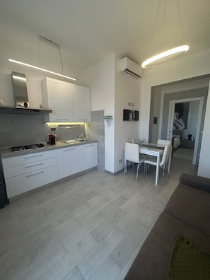 A modern kitchen with white cabinetry, a gas stove, and a dining area with a glass table and white chairs. - Apartment with a private pool and garden, just a few minutes from the beach (Pietrasanta)