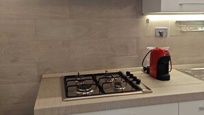 Uma cozinha com coifa de aço inoxidável, fogão a gás e chaleira vermelha.